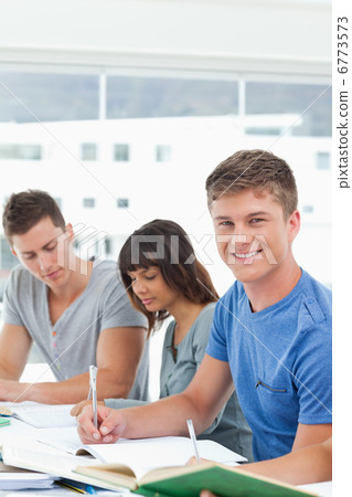 A man looks up from studying into the camera and smiles 6773573