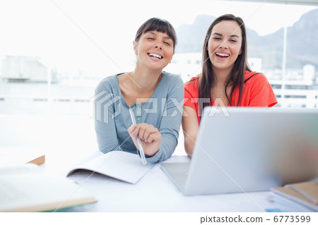 Two laughing girls sitting in front of a laptop together as they 6773599