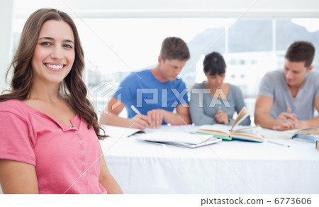 A smiling woman sits in front of her three friends who are study A smiling woman sits in front of her three friends who are study 6773606