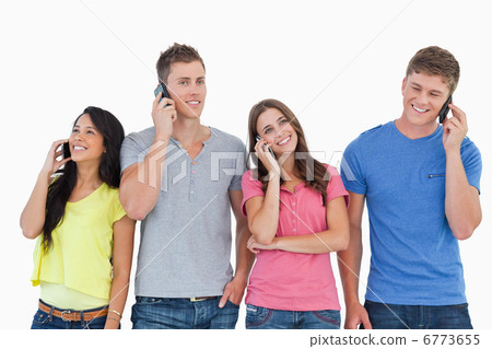 Four people all on their phones as they stand beside each other Four people all on their phones as they stand beside each other 6773655