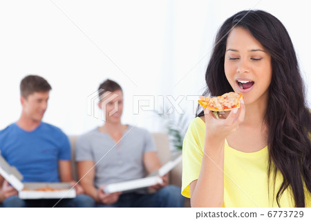 Woman about to eat a pizza slice as her friends sit behind her 6773729