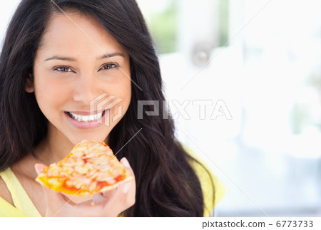 A smiling woman holding a slice of pizza as she looks at the cam 6773733