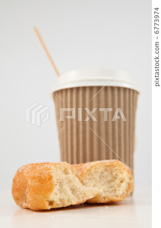 An half eaten doughnut and a cup of tea placed together 6773974