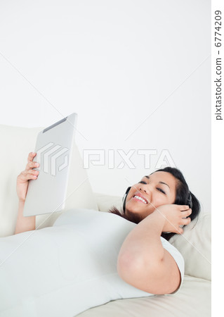 Woman lies on a sofa with headphones on and holding a tactile ta Woman lies on a sofa with headphones on and holding a tactile ta 6774209