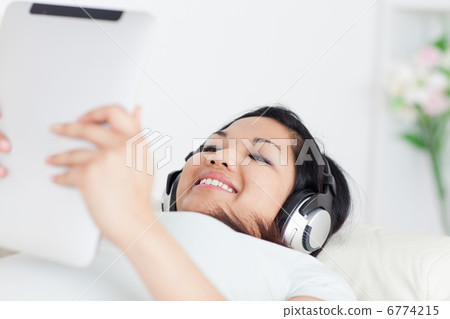 Smiling woman lying on a coach with headphones on and holding a 6774215