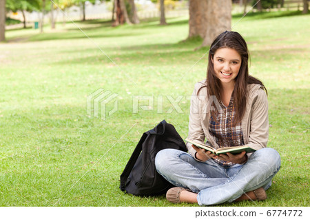 Smiling teenager sitting while holding a textbook 6774772
