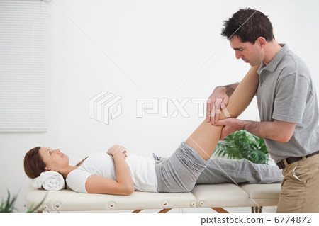 Physiotherapist massaging a leg while placing it on his shoulder Physiotherapist massaging a leg while placing it on his shoulder 6774872