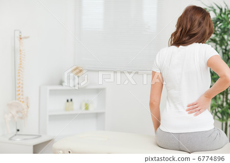Woman sitting on a table while touching her back 6774896