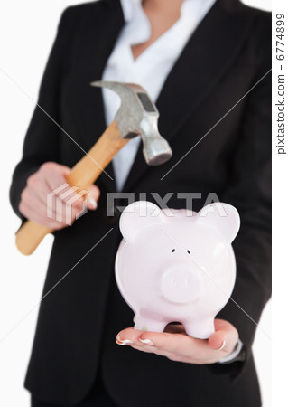 Businesswoman holding a piggy-bank and a hammer Businesswoman holding a piggy-bank and a hammer 6774899