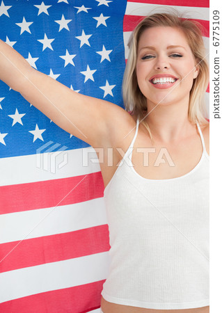 Cheerful blonde woman raising the Stars and Stripes flag 6775109