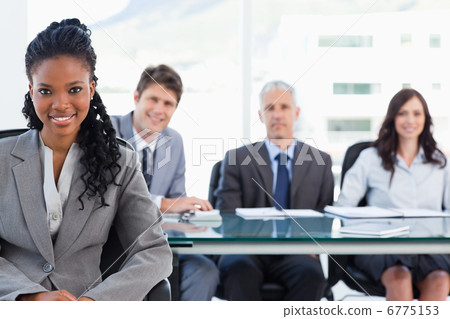 Serious businesswoman sitting in front of her team while smiling Serious businesswoman sitting in front of her team while smiling 6775153