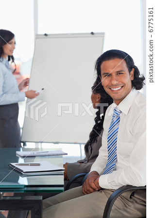 Smiling businessman sitting at a desk while listening to a prese Smiling businessman sitting at a desk while listening to a prese 6775161