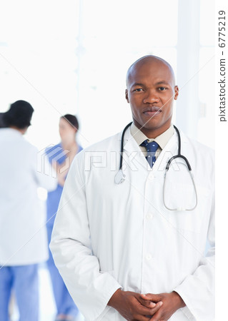 Doctor standing upright with his hands crossed and his team in t Doctor standing upright with his hands crossed and his team in t 6775219