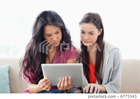 Two women on the couch looking at a tablet together Two women on the couch looking at a tablet together 6775343