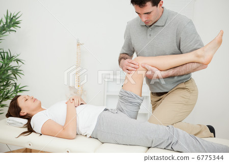 Serious osteopath bending the leg of a patient Serious osteopath bending the leg of a patient 6775344