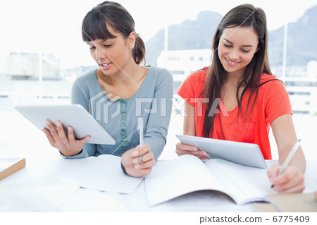 Two girls both using tablet pcs to do their homework Two girls both using tablet pcs to do their homework 6775409