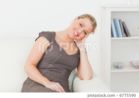 Woman sitting on a sofa while holding her head with her hand Woman sitting on a sofa while holding her head with her hand 6775590