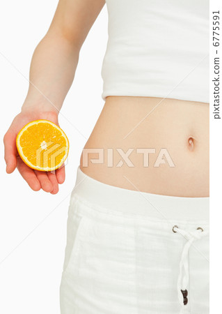 Close up of a woman placing an orange near her belly Close up of a woman placing an orange near her belly 6775591