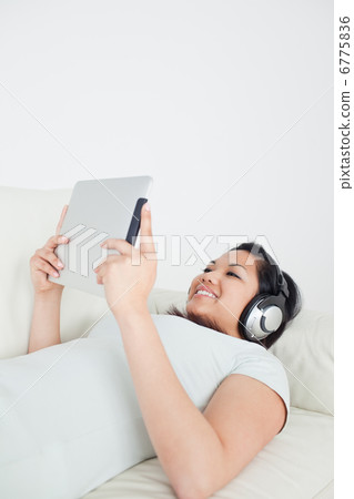 Woman lying on a sofa with headphones on and holding a tactile t Woman lying on a sofa with headphones on and holding a tactile t 6775836