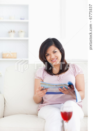Woman holding a magazine and sitting on a couch Woman holding a magazine and sitting on a couch 6775837