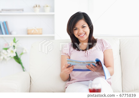 Woman sitting on a sofa while holding a magazine Woman sitting on a sofa while holding a magazine 6775839
