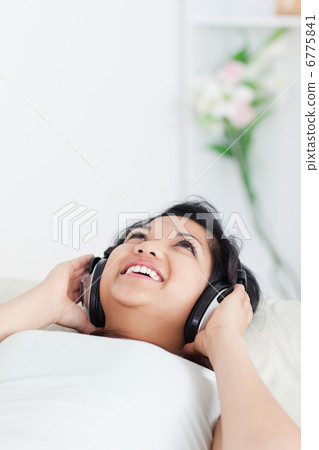 Smiling woman lying on a couch with headphones on Smiling woman lying on a couch with headphones on 6775841