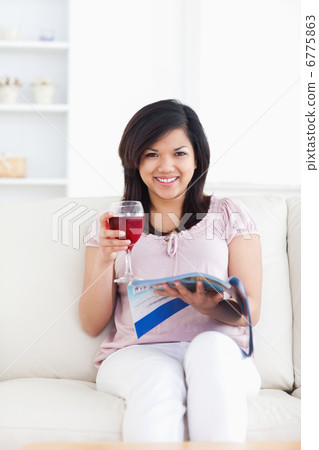 Woman looking ahead as she reads a magazine and holds a glass of Woman looking ahead as she reads a magazine and holds a glass of 6775863