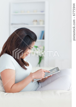 Woman sitting on a sofa while holding a tablet Woman sitting on a sofa while holding a tablet 6775944
