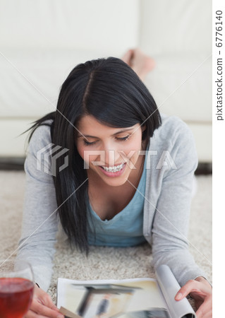Woman smiling while lying on the floor and reading a magazine Woman smiling while lying on the floor and reading a magazine 6776140
