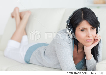 Woman thinking with headphones on while laying on a couch 6776141