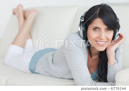 Woman smiling with headphones on while lying on a sofa Woman smiling with headphones on while lying on a sofa 6776144