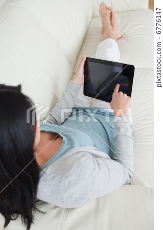 Woman lying on a sofa while touching a tactile tablet 6776147