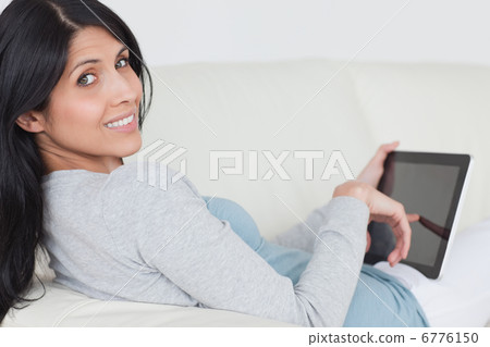 Woman touching a tablet screen while sitting on a couch Woman touching a tablet screen while sitting on a couch 6776150