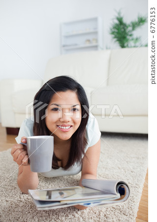 Woman holding a magazine as she lays on the floor Woman holding a magazine as she lays on the floor 6776153