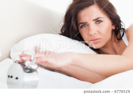 Serious woman switching off her alarm clock 6776529