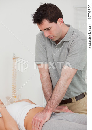 Serious physiotherapist manipulating the pelvis of a patient 6776791