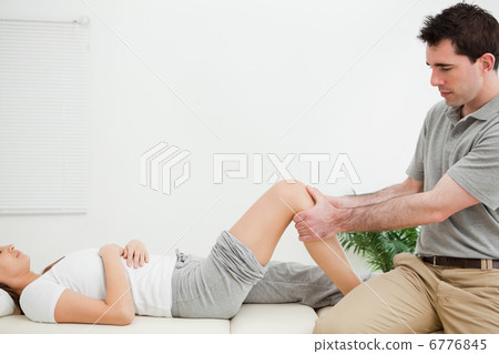 Physiotherapist sitting while massaging a knee 6776845