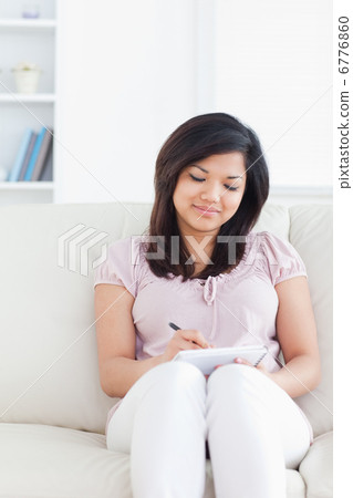 Woman writing on a notebook while sitting on a couch Woman writing on a notebook while sitting on a couch 6776860