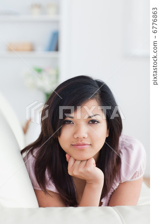 Woman holding her head with her fist while resting on a couch 6776863