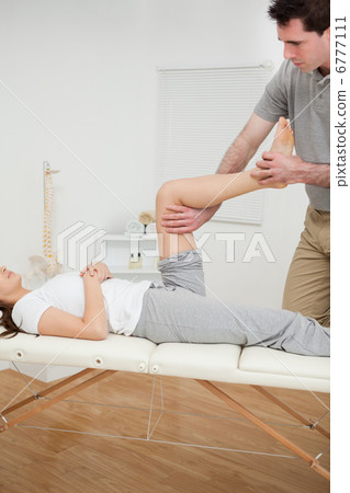 Serious osteopath bending the leg of a woman Serious osteopath bending the leg of a woman 6777111