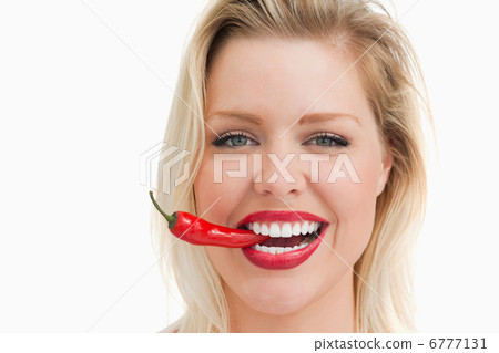 Happy woman biting a red chili while standing Happy woman biting a red chili while standing 6777131