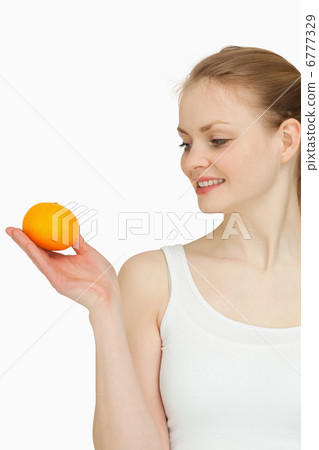 Smiling woman presenting a tangerine while looking at it Smiling woman presenting a tangerine while looking at it 6777329