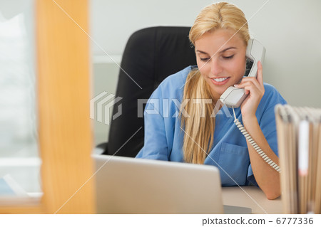 Blonde nurse calling next to a laptop Blonde nurse calling next to a laptop 6777336