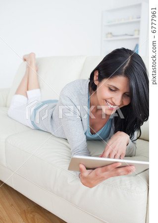 Smiling woman lying on a couch and plays with a tactile tablet Smiling woman lying on a couch and plays with a tactile tablet 6777961