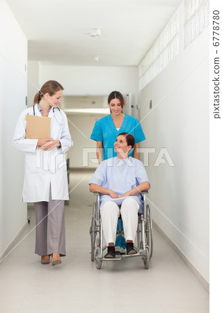 Nurse pushing a patient in a wheelchair while talking to a docto 6778780