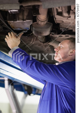 Mechanic repairing the below of a car with a spanner 6779497