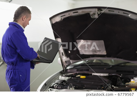 Man typing on a computer next to a car 6779567
