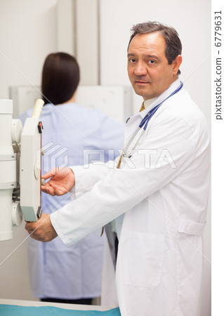 Doctor checking a machine while a patient is having a mammograph 6779631