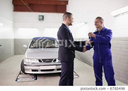 Mechanic giving car key while shaking hand to a client Mechanic giving car key while shaking hand to a client 6780496