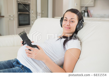 Prospective mother lying on the couch listening to music and hol 6831554